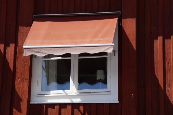 Röd fönstermarkis monterad på ett rött trähus med vita knutar i Hyltebruk.